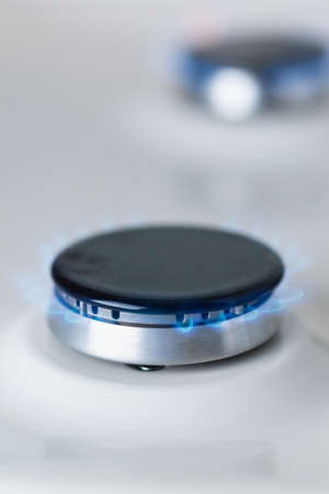 Close-up of a black burner of a white enameled gas stove with a blue fire