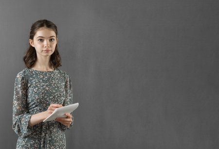 A beautiful successful girl in a dress stands against a gray wall with a notebook and pen in her hands. Copy spaceの写真素材