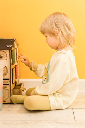 A beautiful little child is sitting on the floor and playing with a developing multifunctional wooden cube. selective focusの写真素材