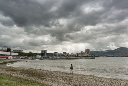 Novorossiysk, Russia, August 13, 2021: A man walks along the rocky shore of Tsemesskaya Bay. Cloudy summer dayのeditorial素材