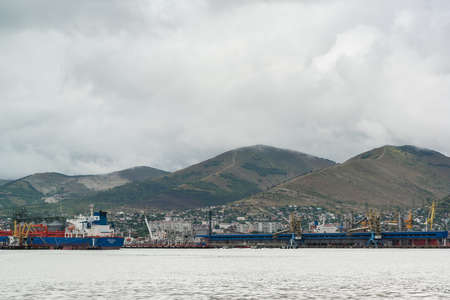Russia, Novorossiysk, August 13, 2021 -Cargo ships and port cranes stand in the port against the backdrop of mountains on a cloudy summer day. Industrial Logistics Centerのeditorial素材