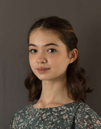 Portrait of a beautiful brunette teenager on a gray background. A slight smile. Generation Z