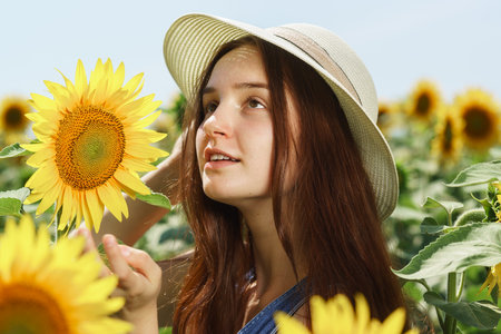 Portrait of a beautiful happy girl with long hair in a white hat in a field with sunflowers. Sunny summerの写真素材