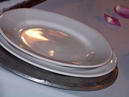 Three plates on a table with pink roses petals, one silver of pewter metal and two white of ceramic