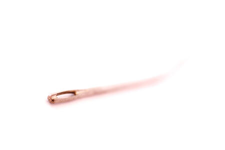 Sewing needle closeup to the hole on abstract blurred white background