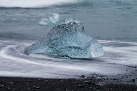 Amazing transparent blue iceberg pieces on Diamond beach with black sand near Jokulsarlon lagoon,...