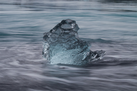 Amazing transparent blue iceberg pieces on Diamond beach with black sand near Jokulsarlon lagoon,...
