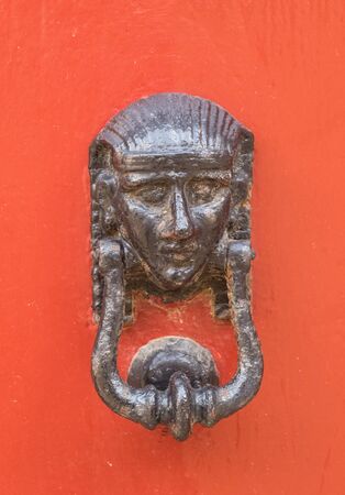 Decorative bronze door handle in the form of a beautiful woman's head on a yellow painted door....