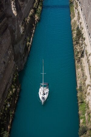 Aerial bird's eye view photo taken by drone of famous Corinth Canal with turquoise water and lonely white yacht , Peloponnese, Greece. The narrowest channel in the world and engineering marvelの写真素材