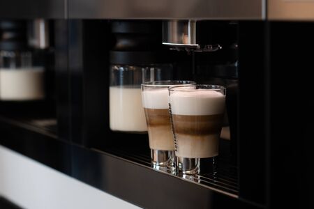 Two glass cuos of cappucino in coffee machineの写真素材
