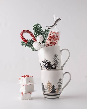 A Christmas sweet gift composition with fir, marshmellow, sweets in a mug on white background.の写真素材
