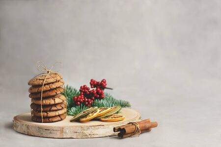 Homemade cookies tied with a rope on a wooden plate with dry orange, cinamon and branch of fir on the side on the grey background.の写真素材