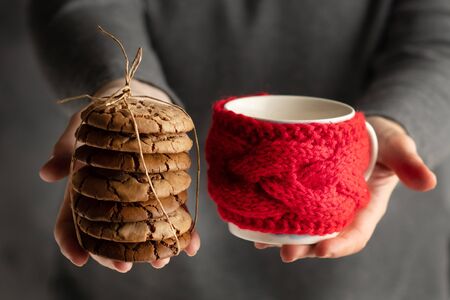 Christmas food. Woman's hands holding a batch of cookies and a cup in red knitted cuo holder.の写真素材
