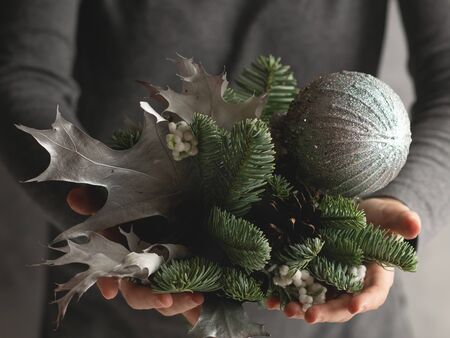 Woman's hands holding branch of fir, silver Christmas balls and silver leaves.の写真素材