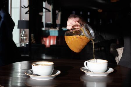 Woman is pouring yellow sea buckthorn tea into a cup in a cafeの写真素材