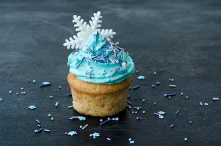 Muffin decorated with cream, pastry topping and snowflake . Cupcake on a wood background. Dessert for Christmas celebration. Festive greeting cardの写真素材