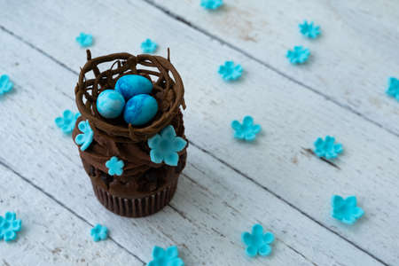 Chocolate easter cupcake with chocolate nest and decorative eggs. Spring flowers. Rustic wood...