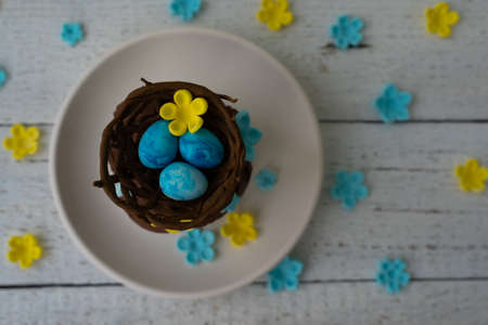 Chocolate easter muffin on plate with chocolate nest and decorative eggs. Spring flowers. Rustic...