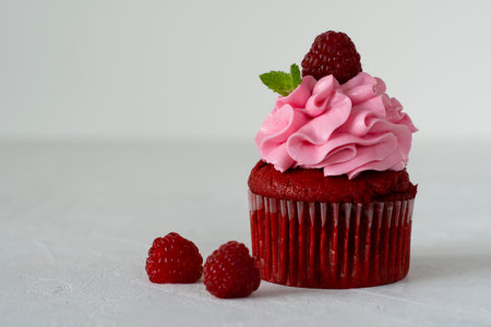 Cupcake red velvet with pink chees cream and raspberries and mint on imitation concrete. Dessert preparation. Copy space. On white background. Delicious delicacy. Muffin with cream. Cake.の写真素材