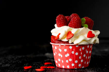 Valentines day cupcake is decorated with raspberries, red hearts on black background. Copy space. Delicious delicacy. Muffin with cream. Cake. low keyの写真素材