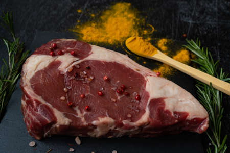 Ribeye raw piece of beef fillet on a slate board and with a spoonful of spilled turmeric, and Himalayan pink salt, pink peppercorns, rosemary. Casually . Macroの写真素材