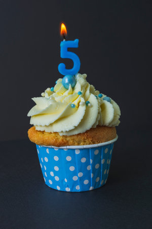 Tasty cupcake with with candles 5 five on a black background. Cake with white cream. Photo in low key. Festive dessert and congratulations.の写真素材