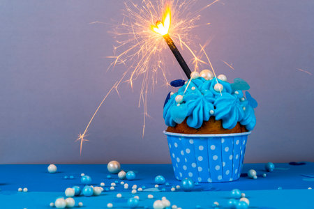 Birthday cupcake with a burning candle, blue background, homemade cakes, ball decorationsの写真素材