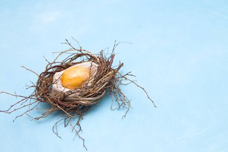 golden easter egg in a makeshift nest of branches on a blue background copy space top view, easter card, place for textの写真素材