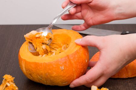  woomen hand with spoon pulls out brush og the pumpkin seeds on the spoon tasty pumpkin and iron knife on the backgrounの写真素材