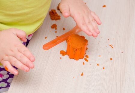 children's hand presses orange sand in a mold for toy muffins and cakes on a beige wooden tableの写真素材