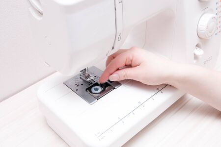 female hand threading the mechanism of the sewing machine, white color and light background