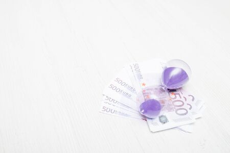 several 500 euro bills on a light background and hourglass with purple sand place copy concept time is moneyの写真素材