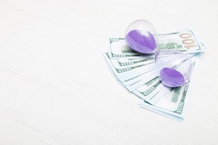 stack of 100 dollar bills and hourglass on a light background copy space