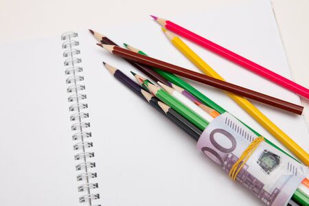 colored pencils wrapped in euro note lie on a white notebook on a white table bright copy spaceの写真素材
