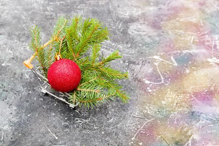 spruce green branch and red shiny Christmas-tree toy ball in a miniature shopping trolley on a black background, copy spaceの写真素材
