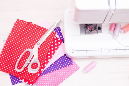 white professional sewing machine on the table, fabrics for girls, scissors and spools of thread,...