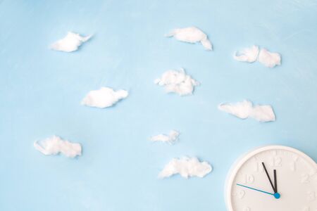 white clock on a blue background with clouds of cotton wool, the concept of time and its waste,...