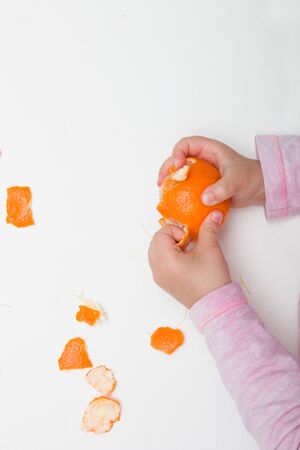 children's hands peel mandarin on a white background pink orangeの写真素材