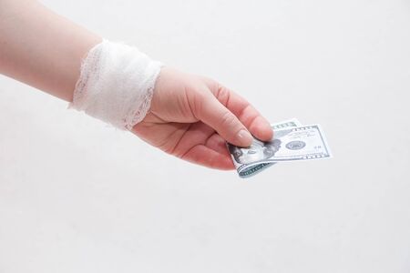 bandaged female hand holds dollar bills on a white backgroundの写真素材