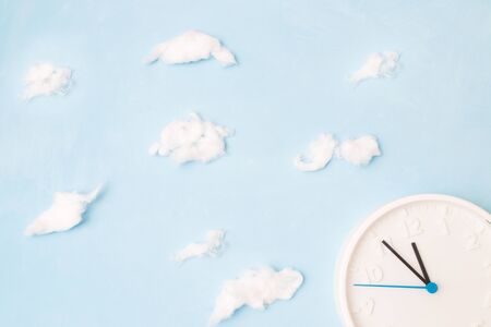 white clock on a blue background with clouds of cotton wool, the concept of time and waste, place copyの写真素材