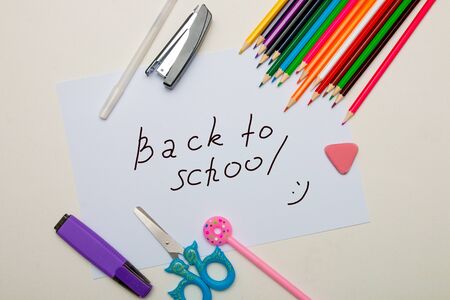 stationery pencils colored highlighter scissors blue childish stapler eraser pen white pink donut on a cap white sheet of paper place copy top view back to schoolの写真素材