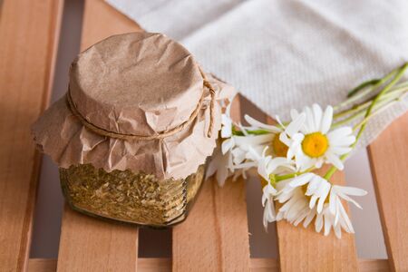 a jar of herbal tea stands on a wooden tray of rekk with a daisy flower and a beige coarse cloth copy space top viewの写真素材
