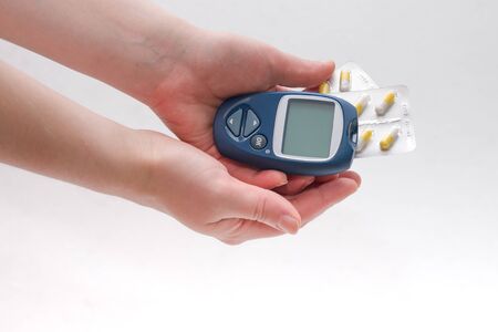 female hand holds a blue glucometer and several packs of tablets of capsules in long colorsの写真素材