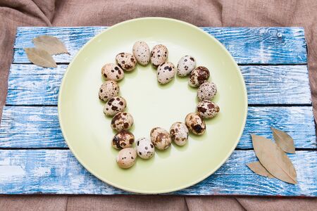 quail eggs laid out in the shape of a heart on a green plate, easter background, blue wooden tray, bay leaf, linen fabric, copy spaceの写真素材