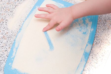 a small child draws a finger with semolina, a kitchen table, the development of fine motor skills, what to do with a child, cutting board blueの写真素材