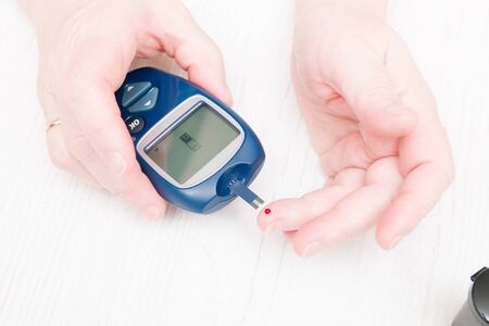 female hands measure blood sugar, a drop of blood on the finger and glucose meter, diabetic do blood test, diabetes conceptの写真素材