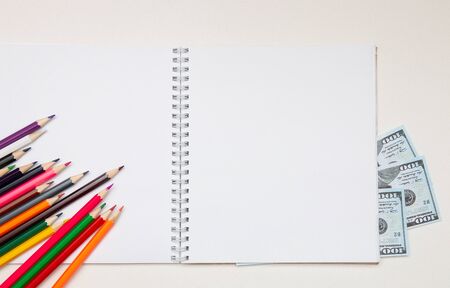 colored pencils lie on a white notebook with a spring and readable sheets of dollars banknotes money on a white table pencil sharpening sharpen color top view spring copybook copy spaceの写真素材