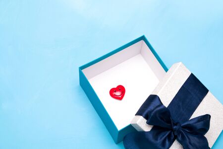 red heart figurine with a smile in a gift box with a large dark blue satin ribbon bow, white box inside, blue background, copy spaceの写真素材
