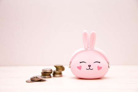 pink silicone wallet in the shape of a rabbit and ears, cute little girl, next to it are stacks of coins, light background, copy space, save love, save money conceptの写真素材