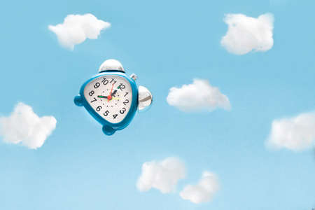 blue alarm clock flies in the clouds of cotton on a blue background, copy space, morning awakening,...